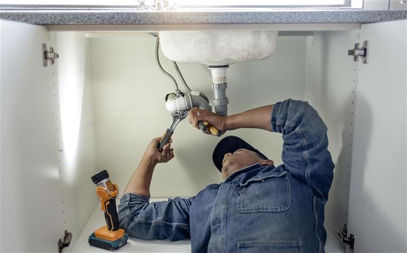 Plumber repairing pipes beneath a bathroom sink in Peachtree City