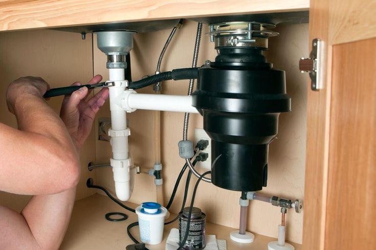 Plumber installing a garbage disposal beneath a kitchen sink in Peachtree City
