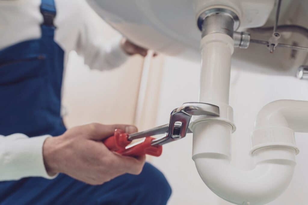 Plumber repairing a white drain pipe beneath a sink in Peachtree City