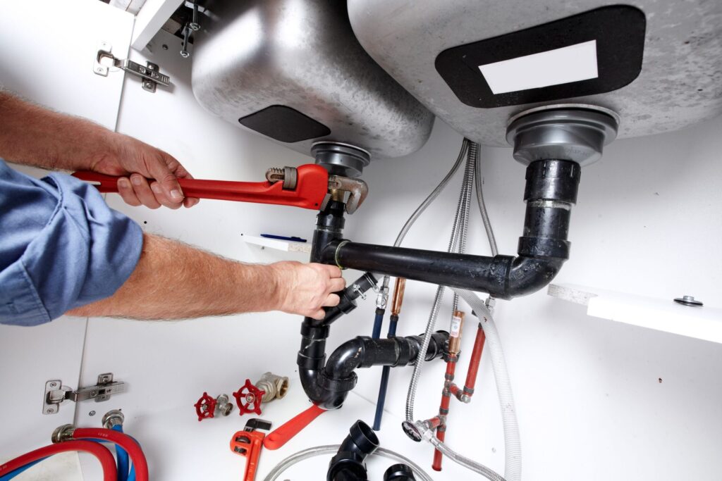 Plumber repairing drain pipes beneath a kitchen sink in Peachtree City